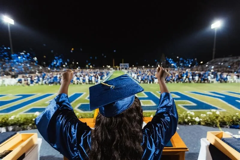 Graduate celebrating under football stadium lights, supplied community image emphasizing future opportunity